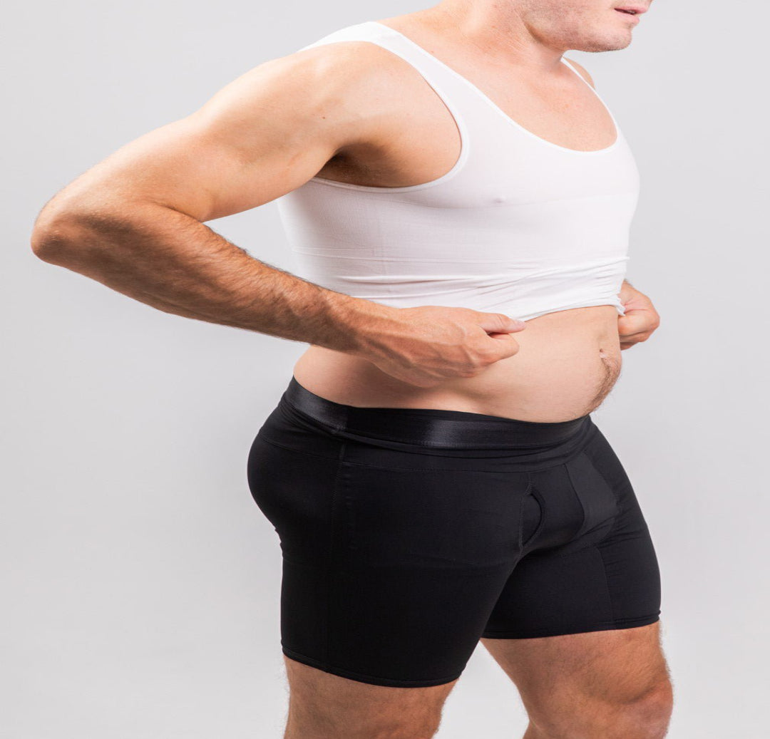 Man wearing a white tank top and black underwear on a plain background